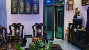 Un salon de style traditionnel, avec des meubles en bois, une grande plante en pot et des œuvres d’art décoratives accrochées au mur.