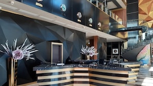 Un espace d’accueil moderne, doté d’un comptoir d’accueil incurvé, d’un escalier en verre et d’un motif géométrique sur le mur.