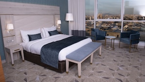 Une chambre d’hôtel moderne dotée d’un grand lit, de tables de chevet, d’un banc et d’un coin salon avec des fauteuils.