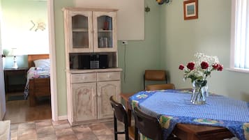 A dining area with a table set for four, a ceiling fan, a cabinet with books, and a window with blinds.