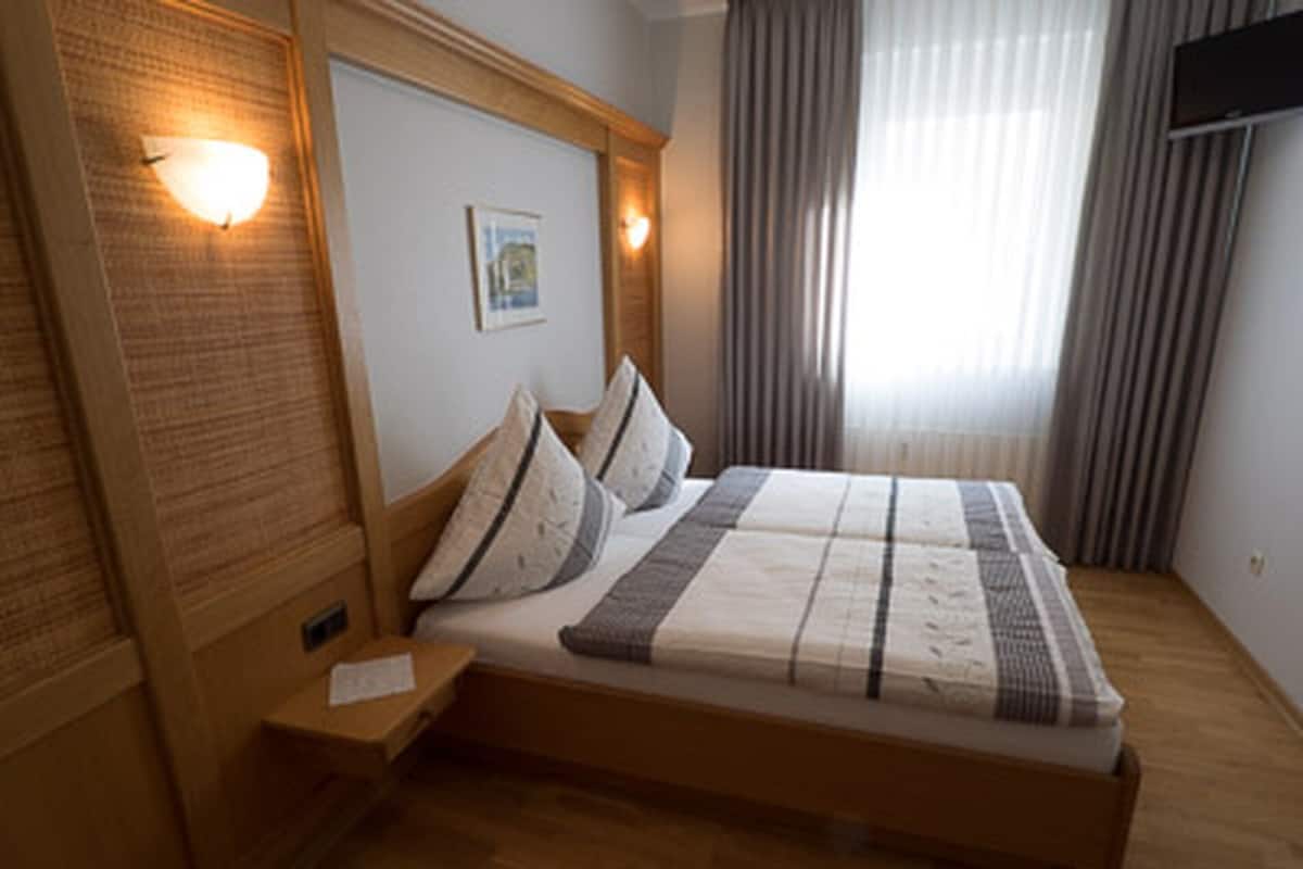 A neatly made bed with pillows and a blanket, a bedside table with a lamp, and a window with curtains.