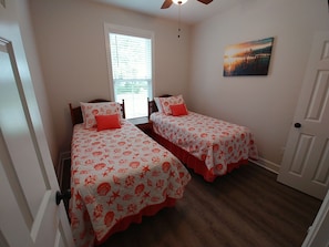 Ein Schlafzimmer mit zwei Betten, jeweils mit einer rot-weißen Bettdecke, einem Fenster mit Rollläden und einem Bild an der Wand.