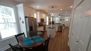 Une cuisine moderne avec des meubles blancs, un îlot central et un coin repas comprenant une table et des chaises en bois.
