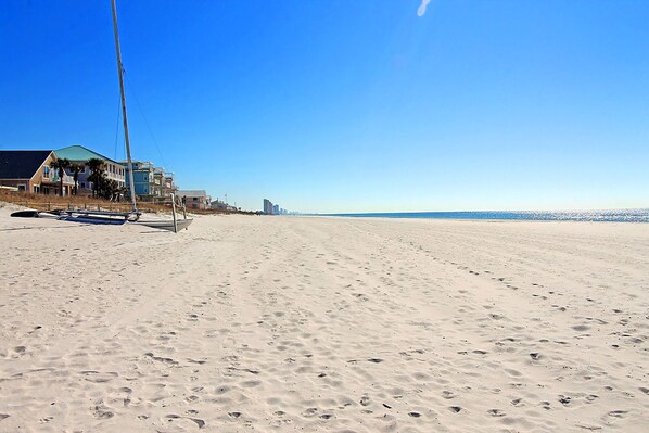 A sandy beach with a sailboat and a house in the background.