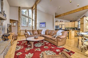 Ein geräumiges Wohnzimmer mit einem großen Ecksofa, einem Holztisch und einem roten Teppich mit Muster.
