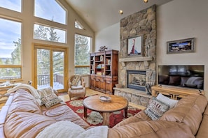 A spacious living room with a stone fireplace, large windows, a comfortable sofa, and a wooden coffee table. - Ski-In/Out Breckenridge Gem w/ Hot Tub! (Breckenridge)