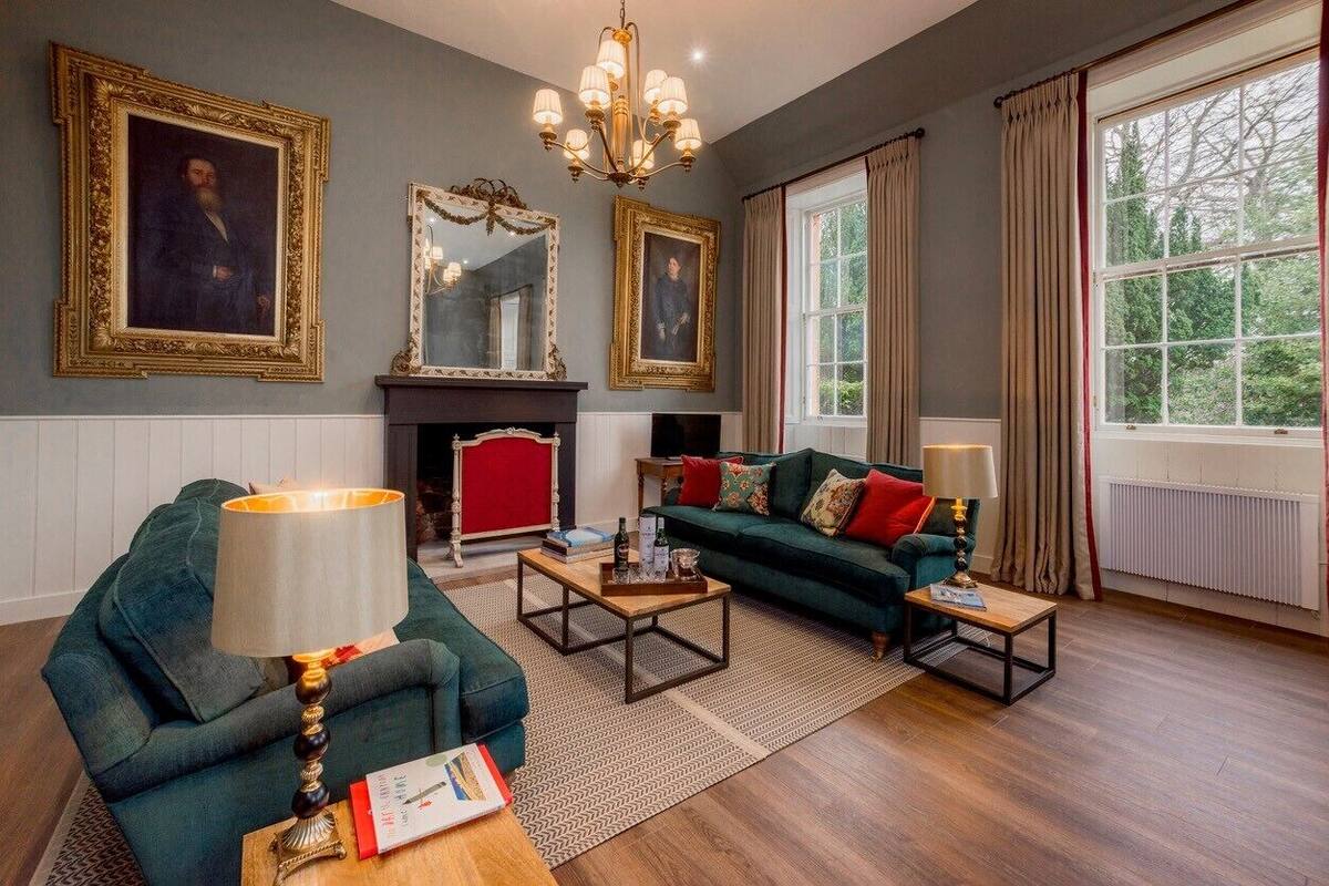 Una sala de estar con chimenea, sofá verde y dos sillones.