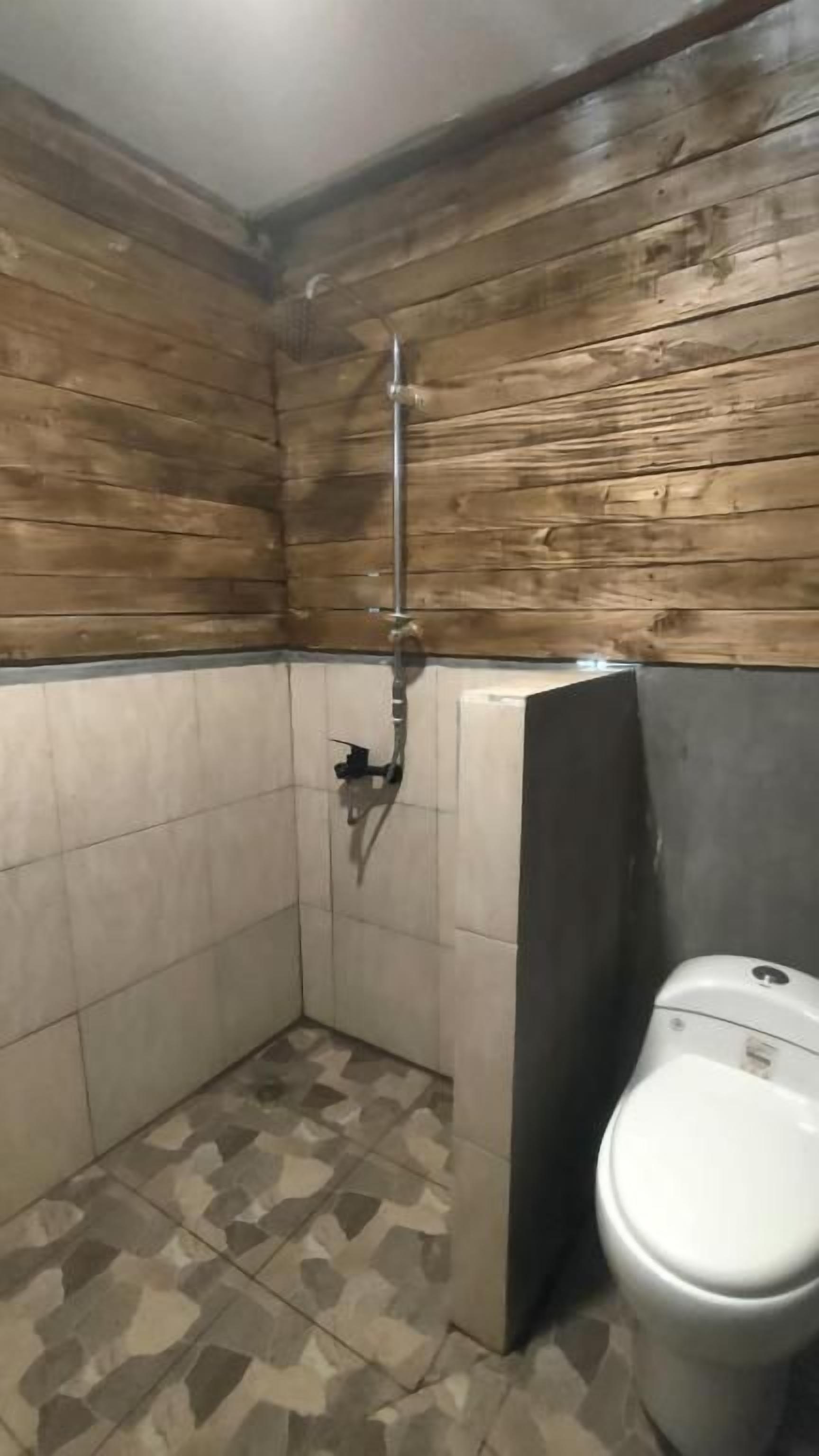 A small bathroom with wooden walls, a tiled floor, and a toilet.