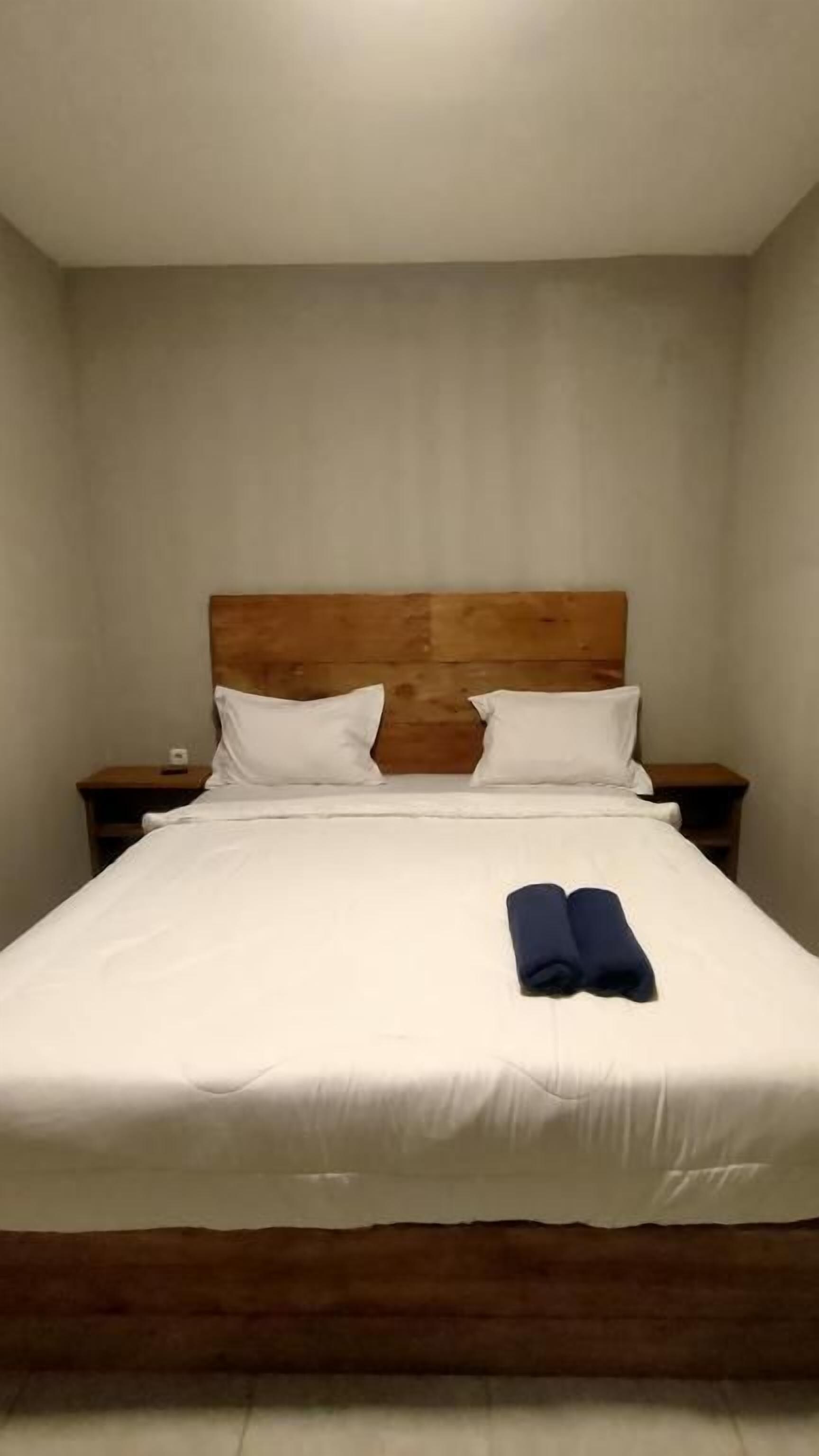 A single bed with a wooden headboard, white bedding, and two pillows.