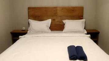 A single bed with a wooden headboard, white bedding, and two pillows.