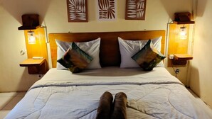 A bed with a wooden headboard, two wall-mounted lamps, and two decorative wall panels. - Angin Mamiri Rinjani Cottages And Resto (Bayan)