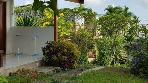 A house with a covered porch, a garden with various plants, and a clear sky. - Angin Mamiri Rinjani Cottages And Resto (Bayan)