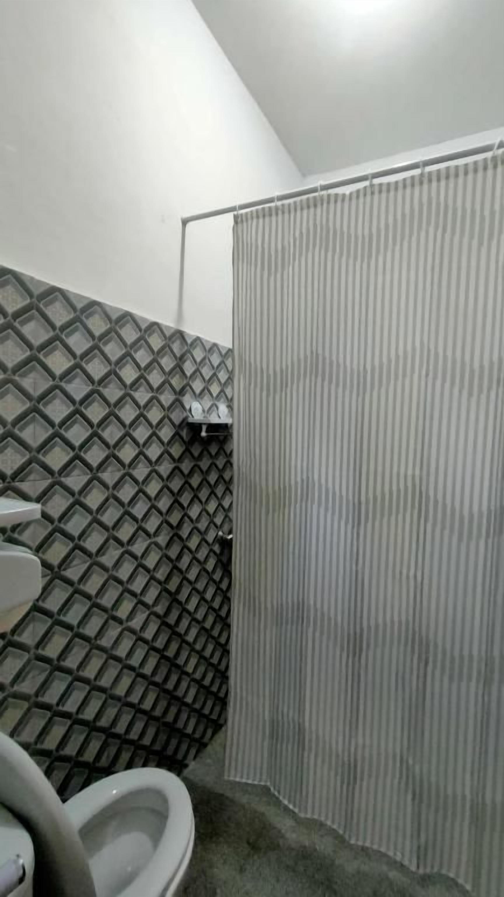 A bathroom with a toilet, a shower curtain, and a tiled wall.