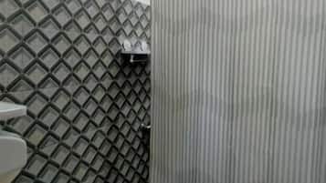A bathroom with a toilet, a shower curtain, and a tiled wall.