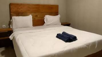 A standard hotel room with a wooden headboard, a single bed with white bedding, and a nightstand with a lamp.