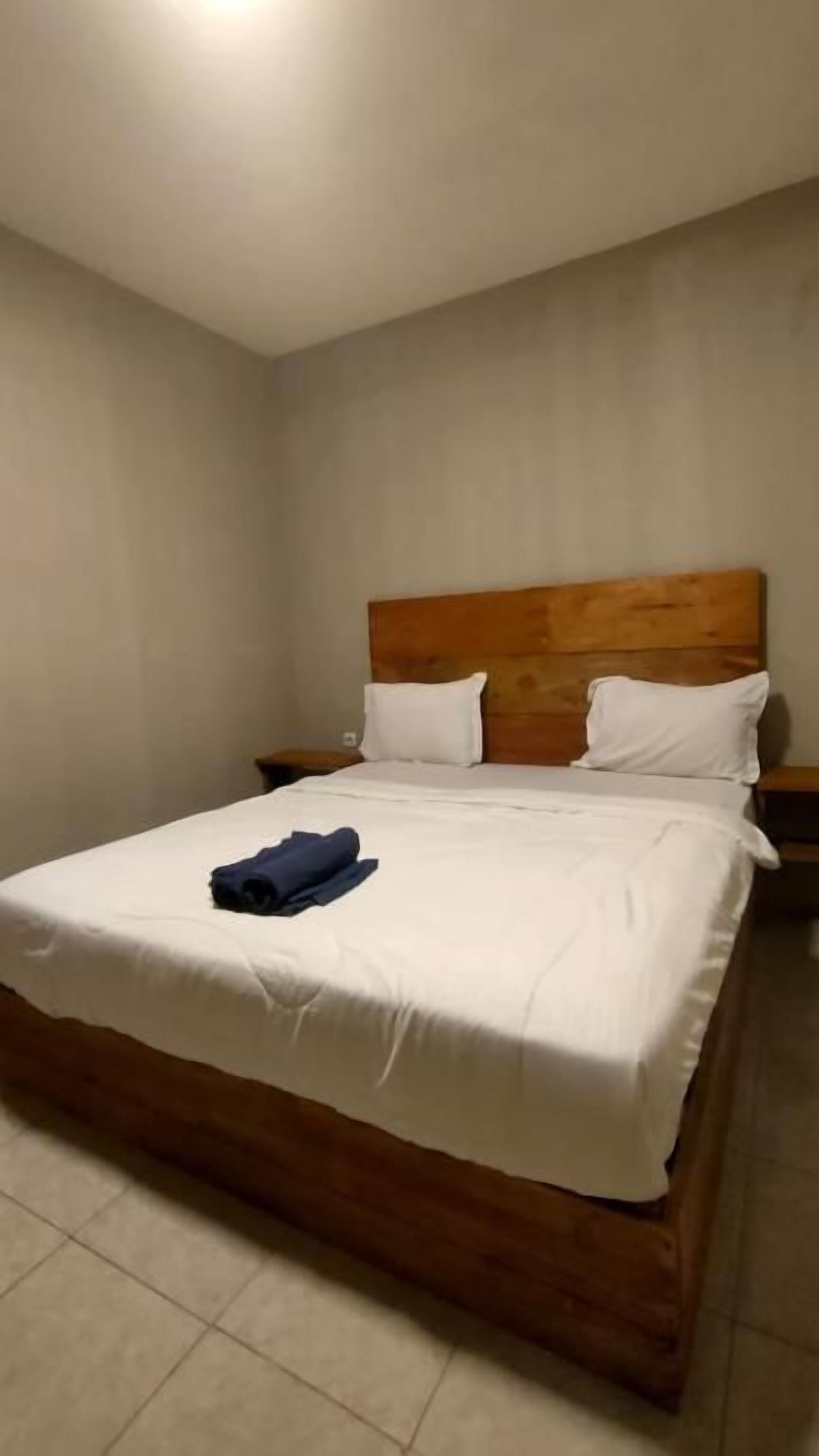 Habitación individual con una cama que tiene cabecera de madera, ropa de cama blanca y una toalla azul sobre la cama.