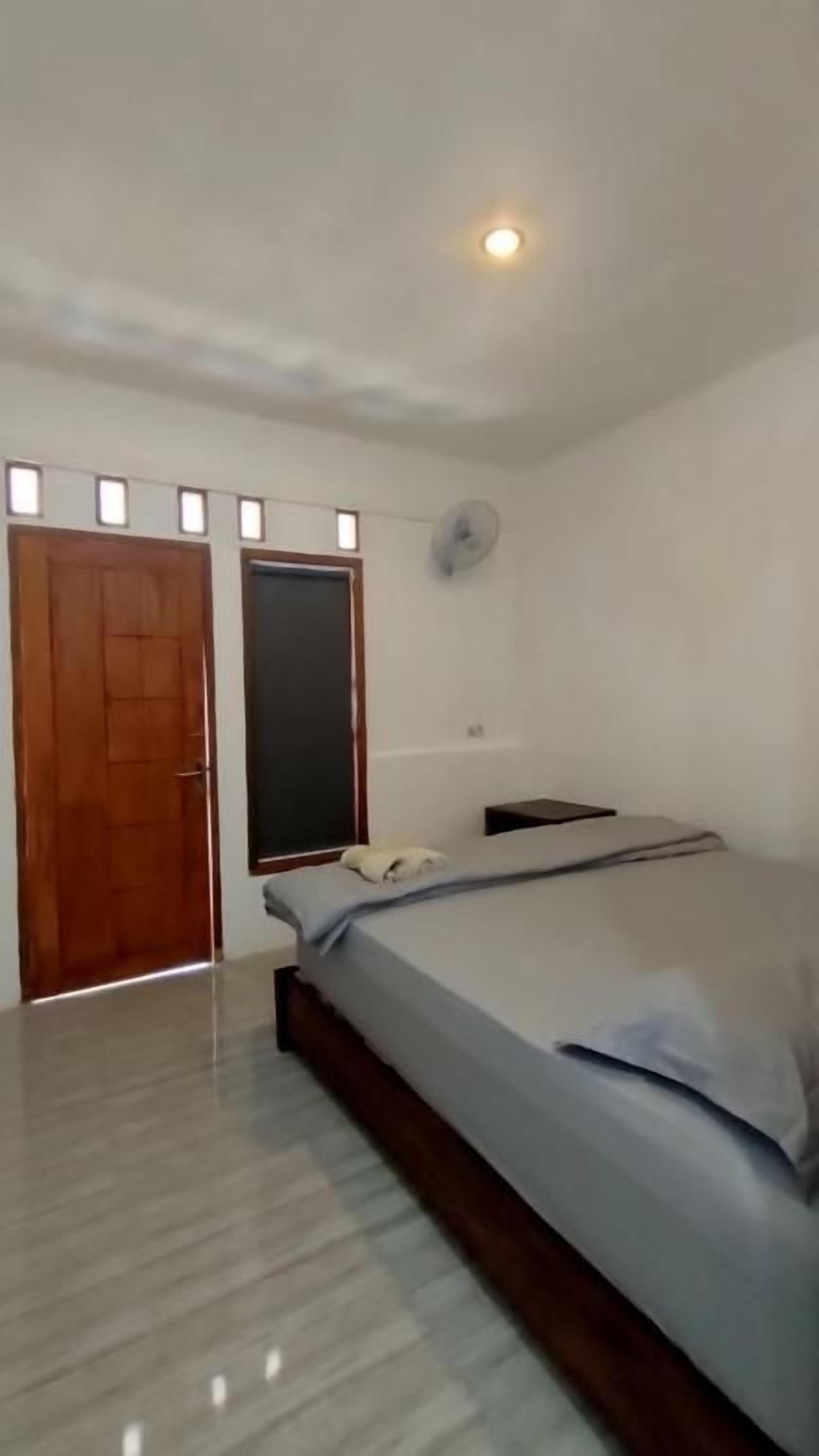 Een slaapkamer met een bed, een houten deur, een ventilator aan de muur en een lamp.