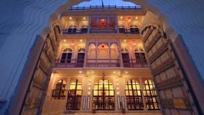 Un immeuble à plusieurs étages, doté de balcons richement décorés et de grandes fenêtres, et dont l’entrée est marquée par un arc imposant.