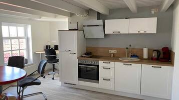 A compact kitchen with white cabinets, a built-in oven, a sink, and a dining area with a red table and black chairs.