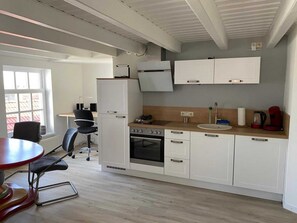 A compact kitchen with white cabinets, a built-in oven, a sink, and a dining area with a red table and black chairs.