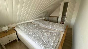 A bedroom with a sloped ceiling, a double bed with patterned bedding, a bedside table, and a small dresser.