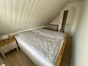 A bedroom with a sloped ceiling, a double bed with patterned bedding, a bedside table, and a small dresser.