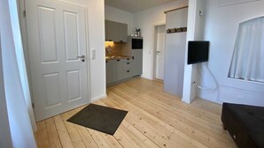 A modern kitchen with white cabinets, a wooden floor, and a black doormat. - Berth 6 - Apartments Meerhuus, 45229 (Jemgum)