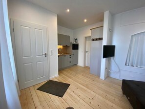 Een moderne keuken met witte kastjes, een houten vloer en een zwarte deurmat.