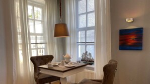 Un coin repas avec une table dressée pour deux personnes, une maquette de bateau sur le rebord de la fenêtre et un tableau accroché au mur.