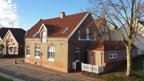 A two-story brick house with a sloped roof, a small attached garage, and a white picket fence.