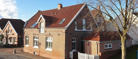 A two-story brick house with a sloped roof, a small attached garage, and a white picket fence.