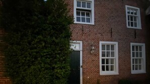 A brick building with a black door, white-framed windows, and a small outdoor light fixture. - Berth 6 - Apartments Meerhuus, 45229 (Jemgum)