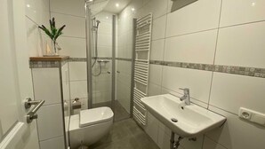 Une salle de bain moderne avec une douche à parois de verre, un lavabo blanc et des toilettes.