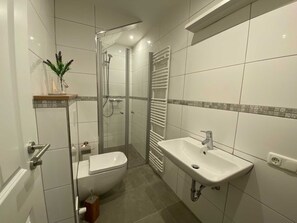 A modern bathroom with a glass-enclosed shower, a white sink, and a toilet.