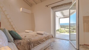 A bedroom with a bed, a ladder, an air conditioning unit, and a view of the countryside through a glass door.