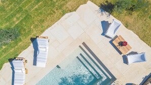 An aerial view of a poolside area with lounge chairs, a wooden table, and a small flower arrangement.