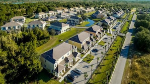 A residential area with single-family homes, a main road, and a body of water in the background. - Vhc7806ha - Serenity - 3 Bed 3 Baths Townhouse (Clermont)