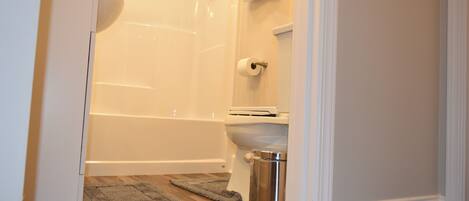 A bathroom with a toilet, a shower, and a trash can.