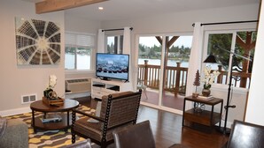Una sala de estar con televisión, un comedor y vistas a un lago a través de amplios ventanales.