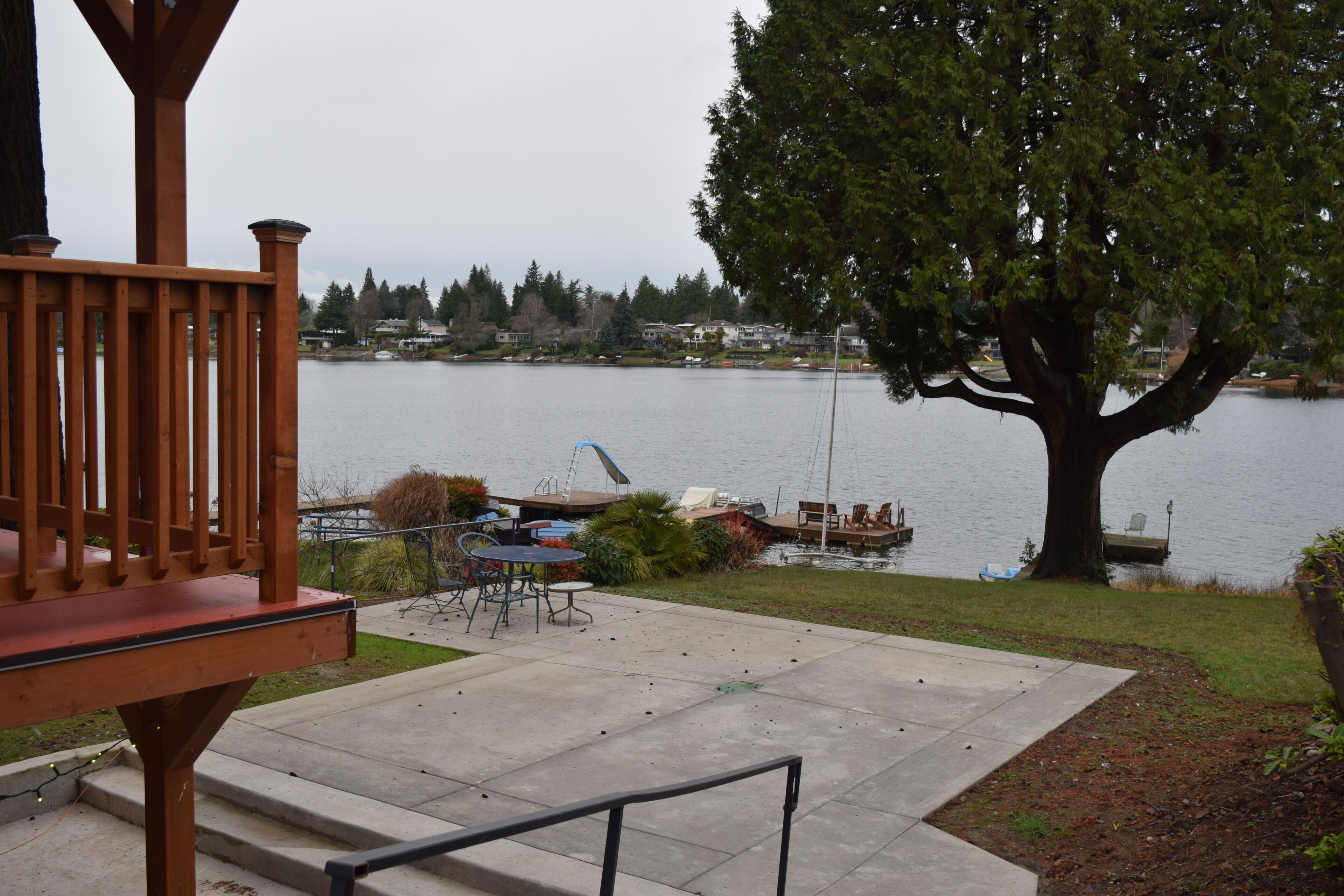 A wooden deck with outdoor furniture, a large tree, and a lake view.