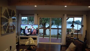 Un salón con televisor, una mesa de centro de madera y vista a un lago a través de amplias ventanas.