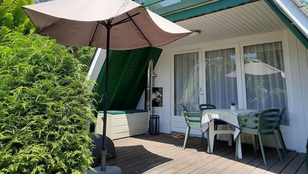 Un espace extérieur abrité, doté d’une table et de chaises, d’un auvent vert et d’une fenêtre avec des rideaux.