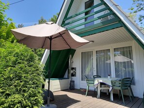 A covered outdoor area with a table and chairs, a green awning, and a window with curtains. - Idyllic Holiday Home in the Palatinate Forest (Gossersweiler-Stein)