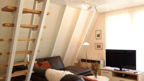 Un salon moderne avec un canapé en cuir noir, une échelle en bois, un téléviseur à écran plat et un plancher en bois.