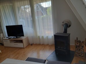 A room with a TV on a wooden cabinet, a fireplace, and a window with sheer curtains. - Idyllic Holiday Home in the Palatinate Forest (Gossersweiler-Stein)