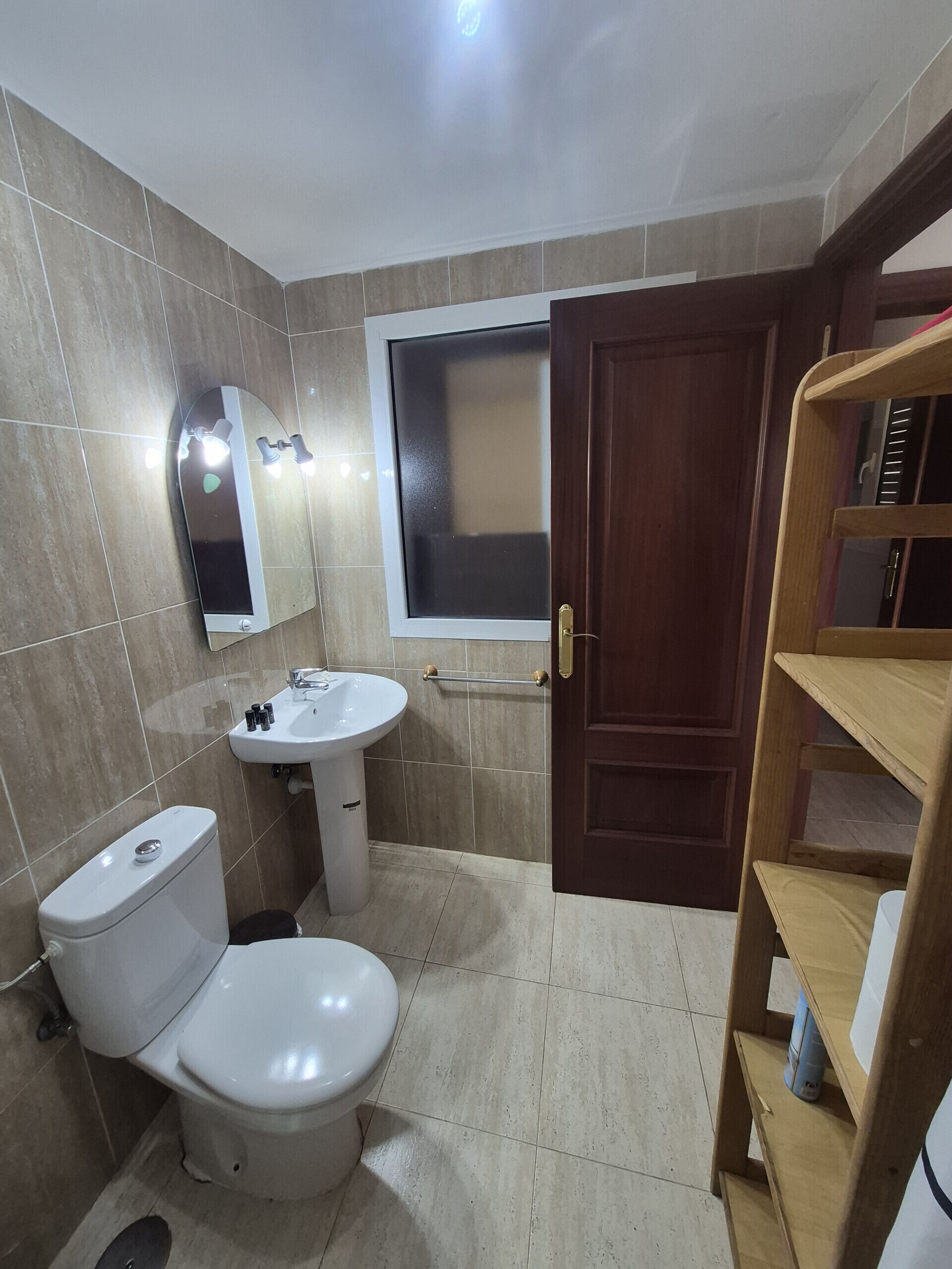 A bathroom with a toilet, sink, mirror, and wooden door.
