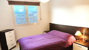 Une chambre à coucher comprenant un lit, une table de chevet, une commode et une fenêtre donnant sur un paysage.