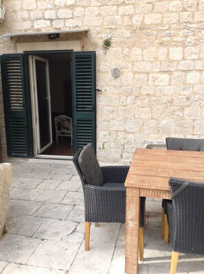 Patio esterno con parete in pietra, mobili in vimini e tavolo in legno.