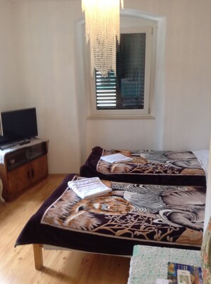 A room with two beds, a wooden cabinet, a television, and a window with blinds.