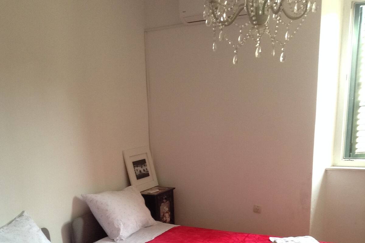A hotel room with two beds, each with a red bedspread and white pillows. There is a small bedside table with a picture frame and a lamp.